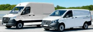 Two white delivery vans parked in a spacious parking lot under a clear blue sky.